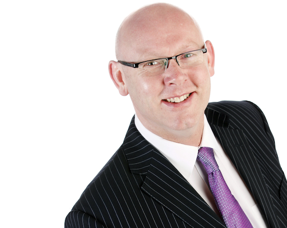 Bruce McLeod smiling, wearing glasses and a suit